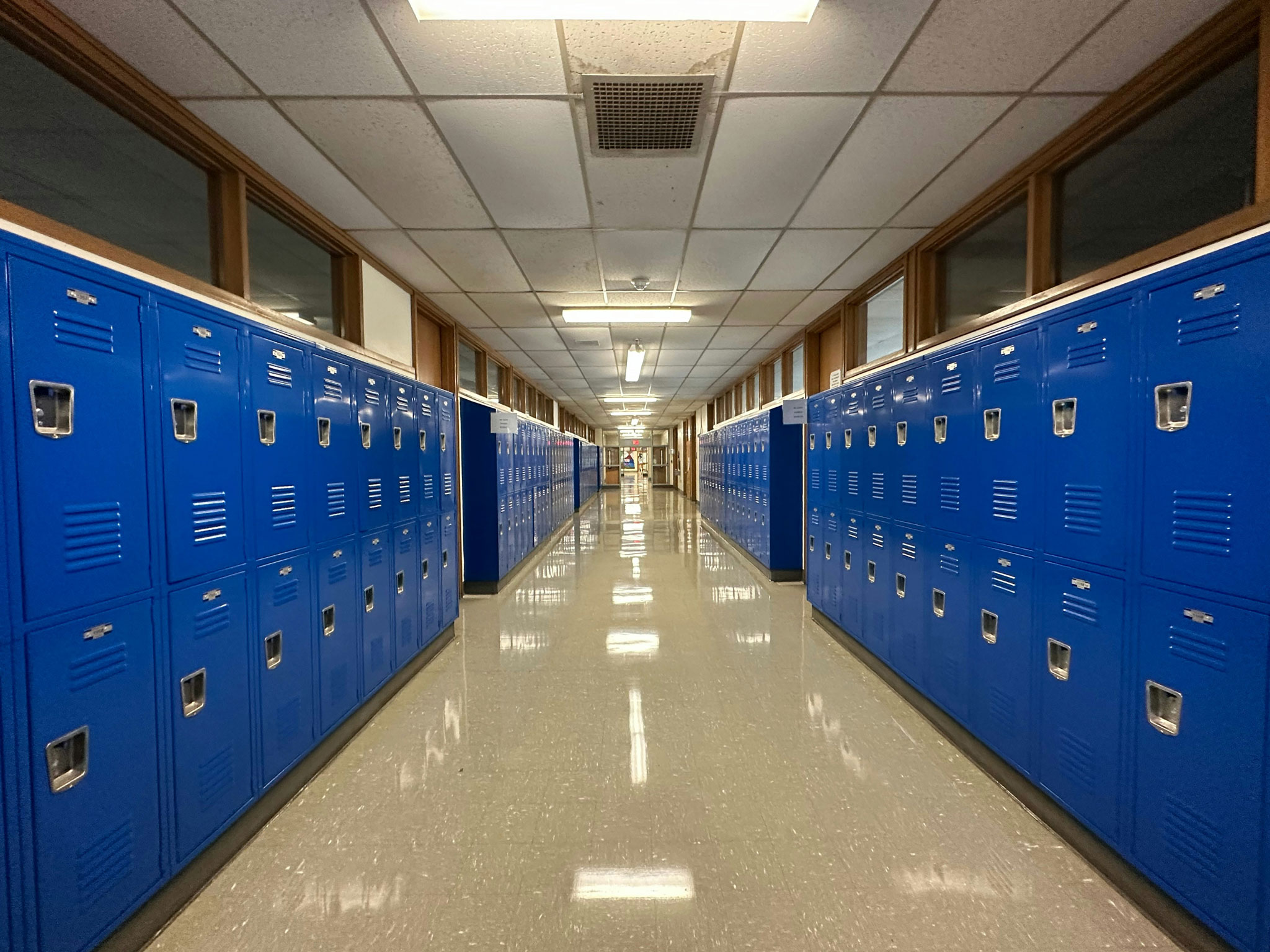 A high school hallway lined with rows of metal lockers under fluorescent lighting